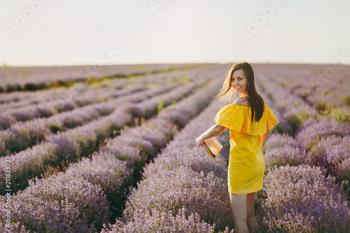 Fototapeta Naklejka Na Ścianę i Meble -  Portrait of young beautiful woman in yellow dress hat on purple lavender flower blossom meadow field outdoors on summer nature background. Female near flowering bush. Lifestyle concept. Back rear view