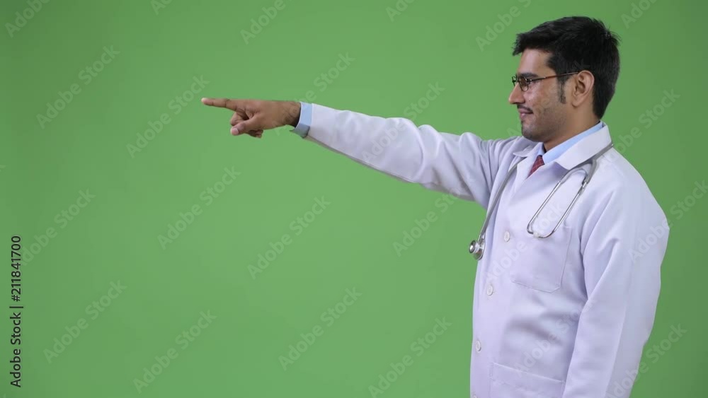 Profile view of young handsome Persian man doctor pointing finger Profile view of young handsome Persian man doctor pointing finger