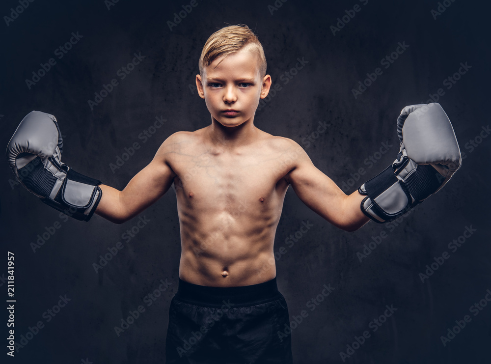 Young shirtless boy boxer with boxing gloves posing in a studio. Isolated on dark textured background.