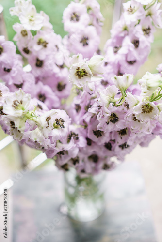 Fototapeta Naklejka Na Ścianę i Meble -  Lilac Delphiniums in glass vase on gray table. Summer wallpaper. Selective focus. Flower shop concept.