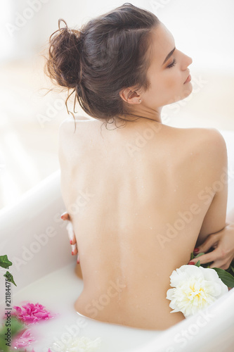 Young beautiful woman taking bath with flowers and milk