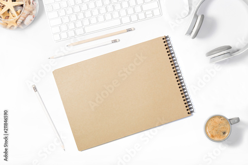 Beautiful light minimalistic mockup. White keyboard, mouse, headphones, pencils, sketchbook, vase with seashells and small cup of coffee on white background. Top view.