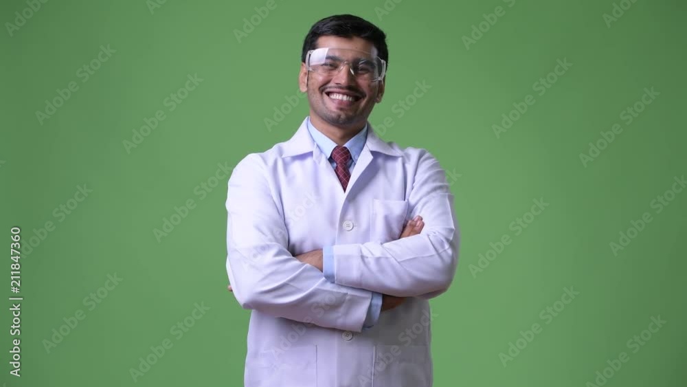 Young handsome Persian man doctor wearing protective glasses with arms crossed Young handsome Persian man doctor wearing protective glasses with arms crossed