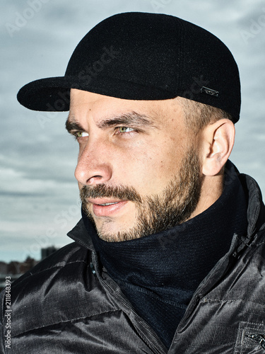 Beautiful portrait of a man in a cap. Cap of different colors and shapes. Autumn portrait, clouds behind and stormy sky. Scarf around the neck in the color of the cap. Face severe, serious.