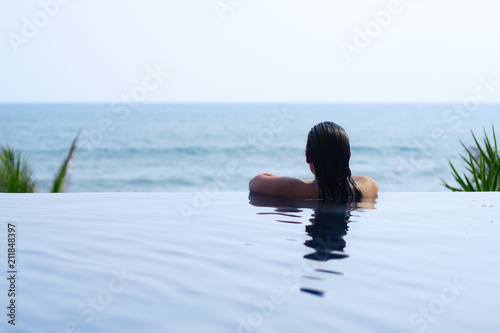 A young woman relaxing in an infinite swimming pool.