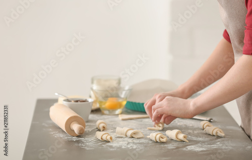 Woman preparing tasty croissants on table in kitchen, closeup