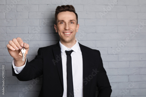 Male real estate agent with key on brick wall background