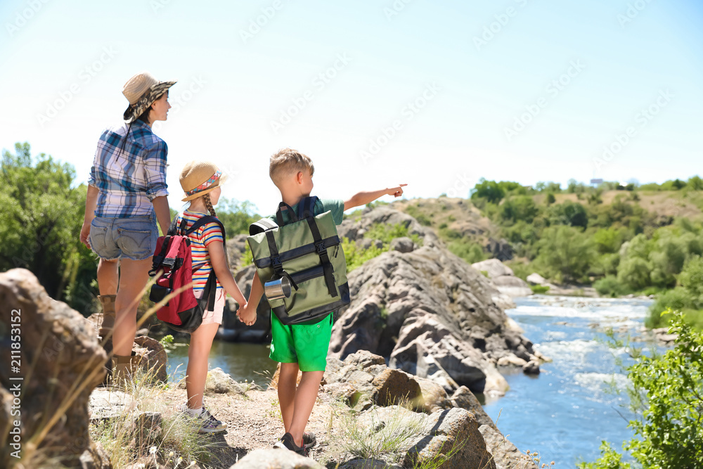 Young woman with children on rock near river. Summer camp