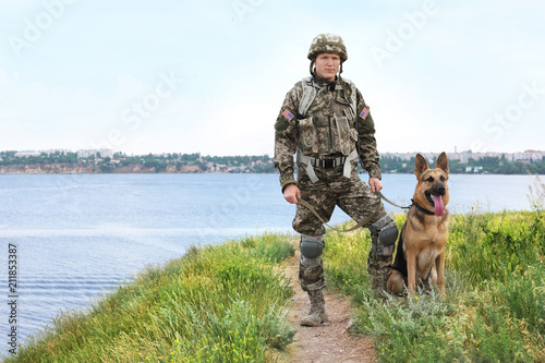 Bilde på lerret Man in military uniform with German shepherd dog near river