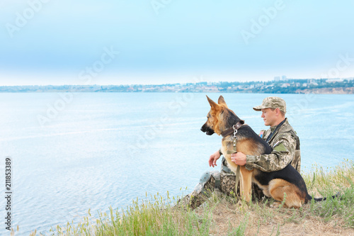 Man in military uniform with German shepherd dog near river