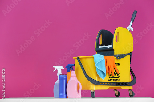 Mop bucket with cleaning supplies on color background