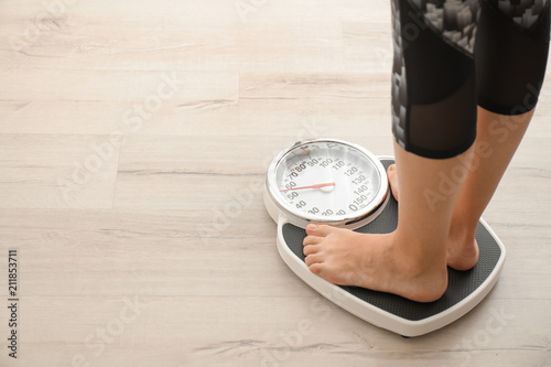 Woman measuring her weight using scales on wooden floor. Healthy diet photo