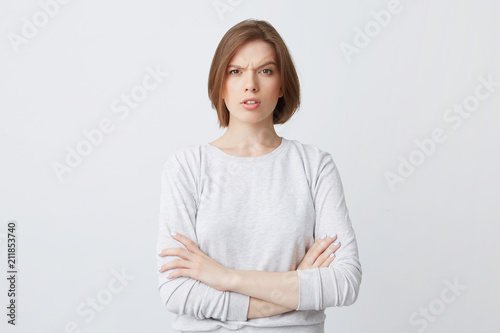 Portrait of serious confused young woman in longsleeve standing with arms crossed and looking confused isolated over white background Feels puzzled photo