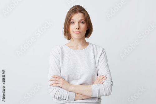 Unhappy dissatisfied young woman in longsleeve standing with hands folded and feels disappointed isolated over white background