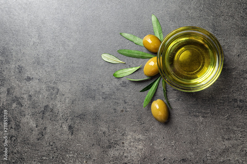 Little bowl with oil, olives and leaves on table, top view