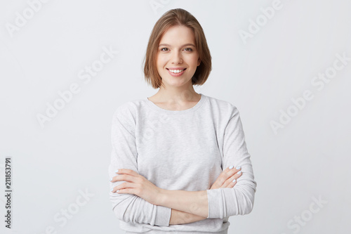 Smiling beautiful young woman in longsleeve standing with arms crossed and feeling confident isolated over white background Looks successful photo