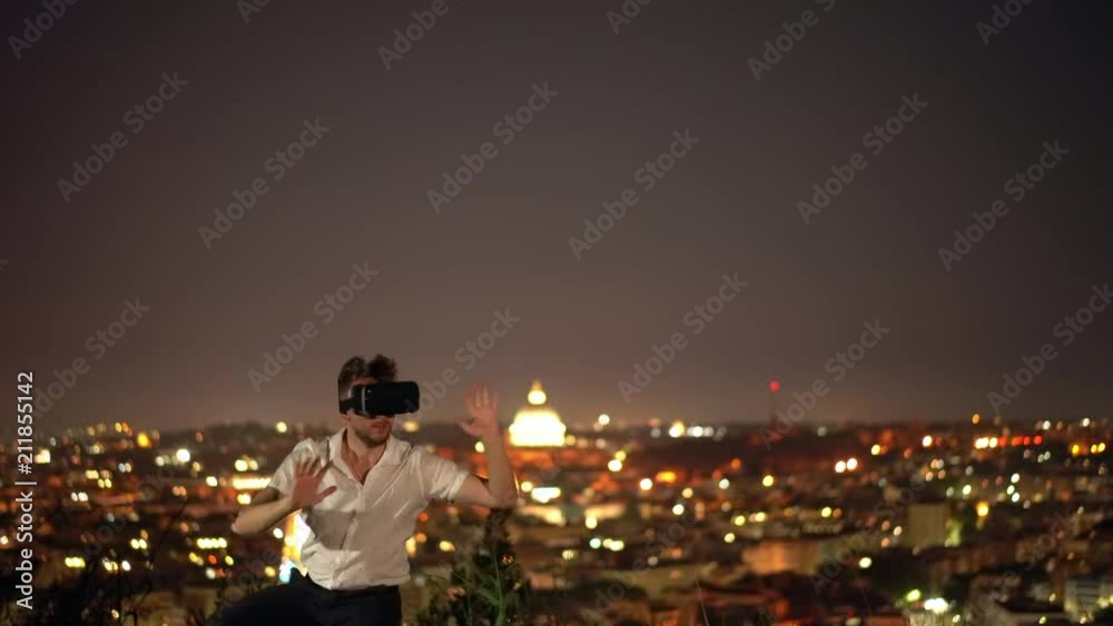 Attractive man Uses glasses of virtual reality against the background of the burning lights of the night city Attractive man Uses glasses of virtual reality against the background of the burning lights of the night city
