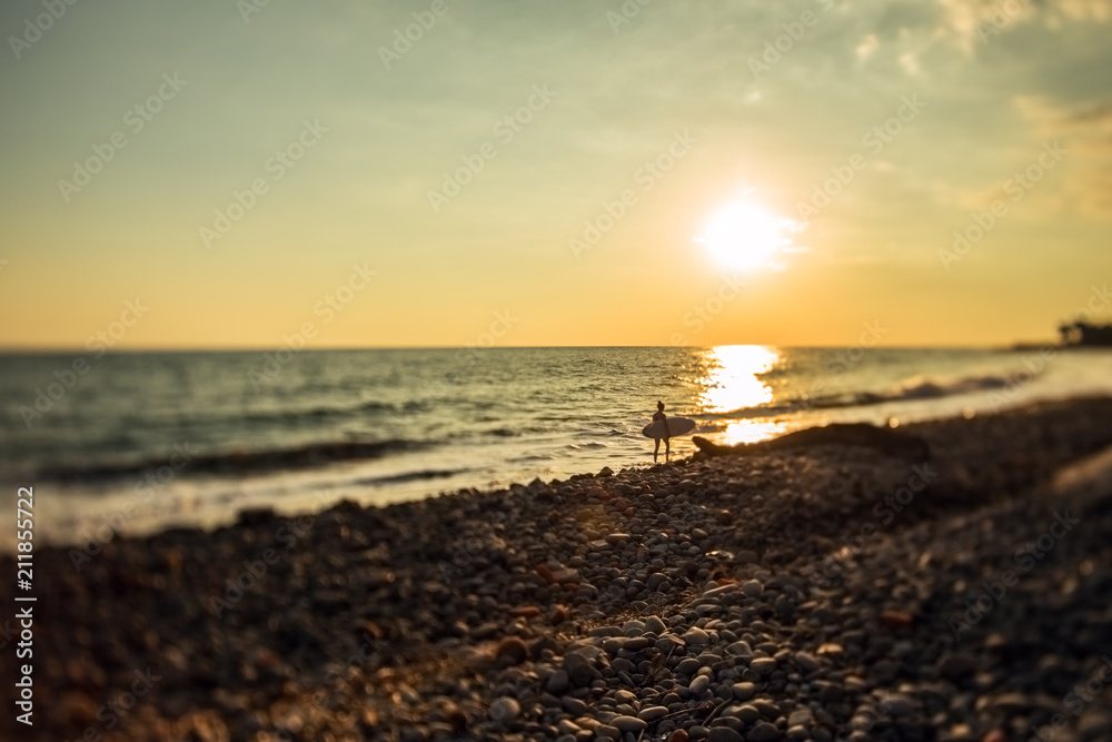 A silhouette of surfer walks by a beautiful sunset in El Sunzal beach at El Salvador taken with a tilt shift lens. A silhouette of surfer walks by a beautiful sunset in El Sunzal beach at El Salvador taken with a tilt shift lens.