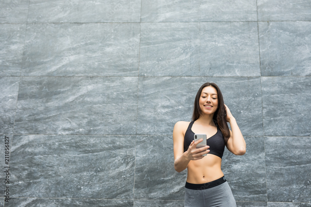 Young woman relaxing after jogging. She using her smart phone Typing message leaning against outdoors wall. Young woman relaxing after jogging. She using her smart phone Typing message leaning against outdoors wall.