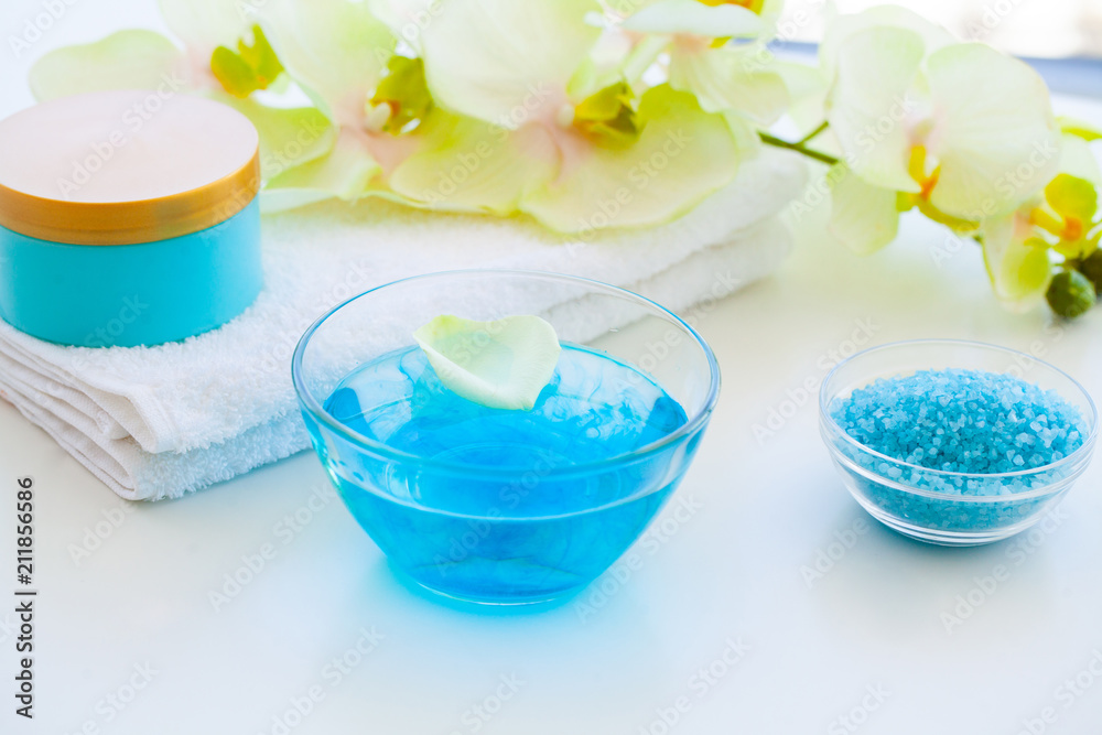 Organic Blue Sea Salt. Spa Composition With Cream, Salt, Towel and Flowers On a White Background. Wellness Products and Cosmetics. Organic Blue Sea Salt. Spa Composition With Cream, Salt, Towel and Flowers On a White Background. Wellness Products and Cosmetics.