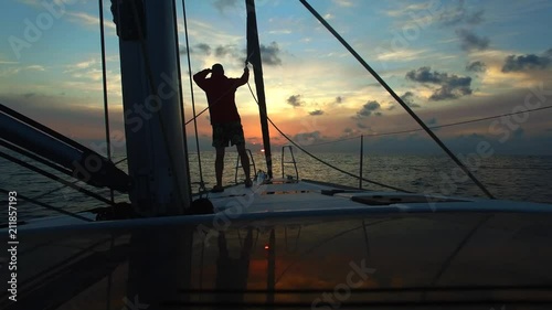 Young man sailor are looking forward on deck sailing yacht at sunset . Freedom on the small ship.