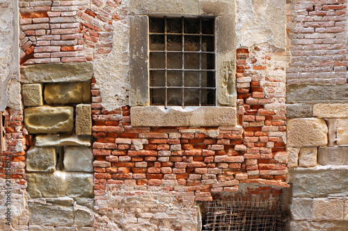 Horizontal photo of an old wall made in different styles, time, materials still standing together and one window with framed by stones in the middle of it 