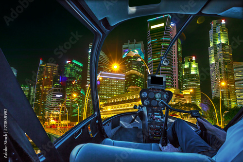 Helicopter interior on Singapore financial buildings and skyscrapers of downtown reflected in the sea of the harbor. Scenic flight above Singapore skyline by night in marina bay promenade waterfront.