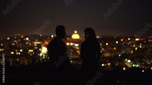The couple sit on a bench on the background of a stars and city lights. Man and woman at night time. Italy, Rome night.