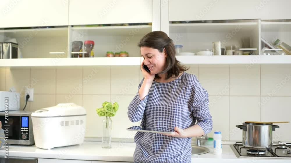 Beautiful young mother taking care of a baby doing kitchen work, cooking, using digital tablet, and having a phone conversation Beautiful young mother taking care of a baby doing kitchen work, cooking, using digital tablet, and having a phone conversation