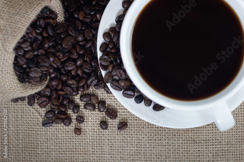 close up concept coffee beans with white cup and saucer on sack background . black and brown color seeds .