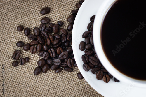 coffee beans with white cup and saucer . black and brown color seeds on sack background .