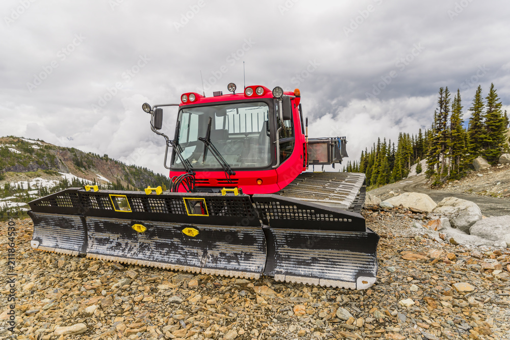 Fototapeta premium Red tractor, snow plough parked outside a mountain on the rocks