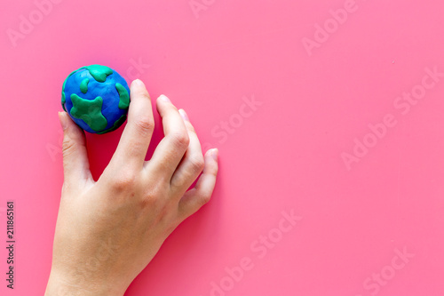Fototapeta Naklejka Na Ścianę i Meble -  Earth. Hand hold plastiline symbol of planet Earth globe on pink background top view copy space