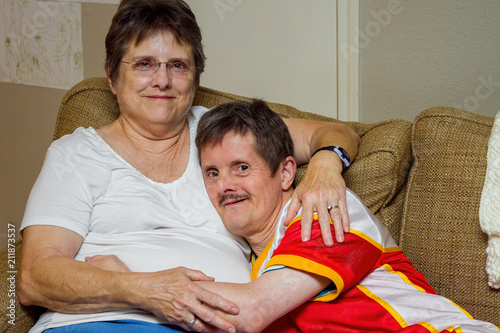 Man With Downs Syndrome Hugs His Older Sister On A Couch