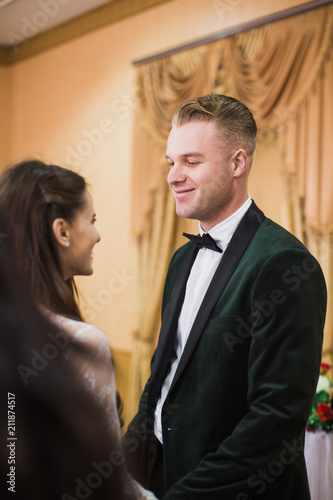 Portrait of the young beautiful couple who is standing indoor and smiling each other and holding hands in their wedding day