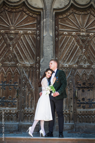 The happy young stylish newlyweds standing in an embrace near the old build