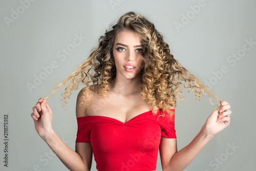 Blonde woman with curly hair. Portrait of positive smiling girl with curly hair isolated on grey background. Makeup and cosmetics for skin care. Beauty and style. Professional hair care.