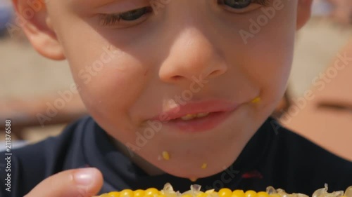 Little hungry boy eating corn on the beach of the sea. Focus on the boiled corn. Close-up.