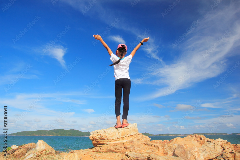 Child girl with arms wide open enjoying the sea,Stand on rock with hand up feel relax or happy or freedom travel,Success and winner concept. Child girl with arms wide open enjoying the sea,Stand on rock with hand up feel relax or happy or freedom travel,Success and winner concept.
