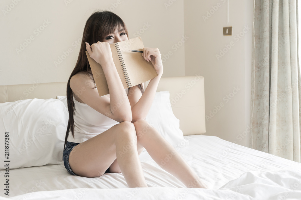 Close up lifestyle soft image of pretty young Asian woman sitting on her cozy bed and making notes to her diary Close up lifestyle soft image of pretty young Asian woman sitting on her cozy bed and making notes to her diary