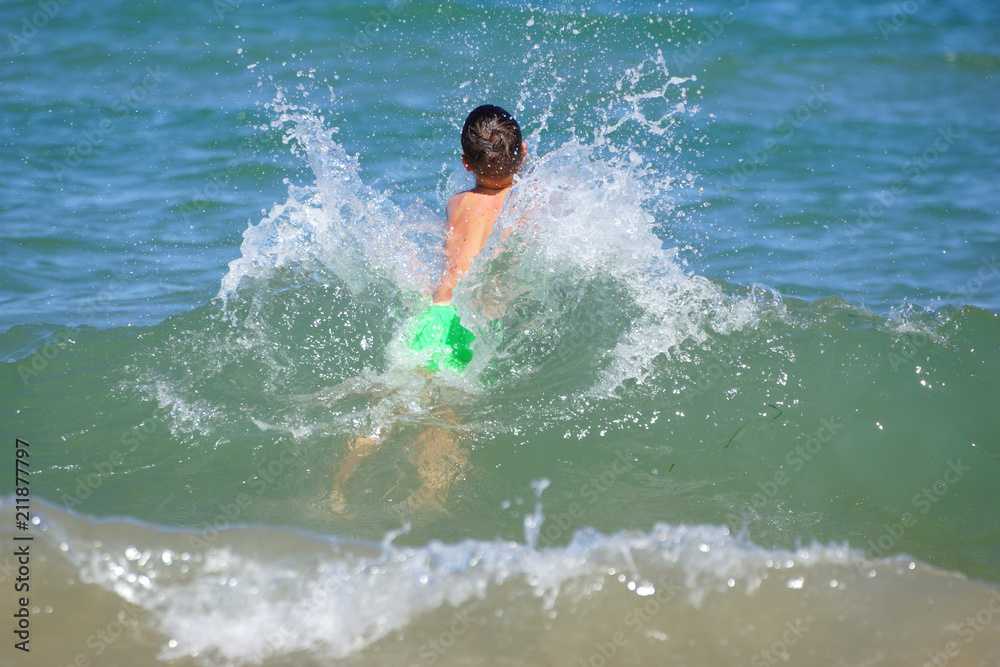 Happy little boy run play with waves on beach of Mediterranean