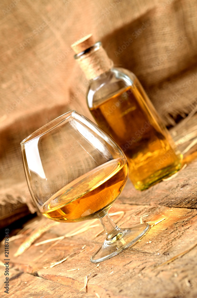 Glass of cognac on rustical wooden background and bottle in background vertical photo