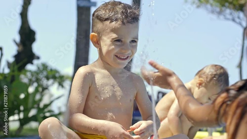 Smiling little boy holding hair band and playing with sister in swimming pool at hot summer day on vacation