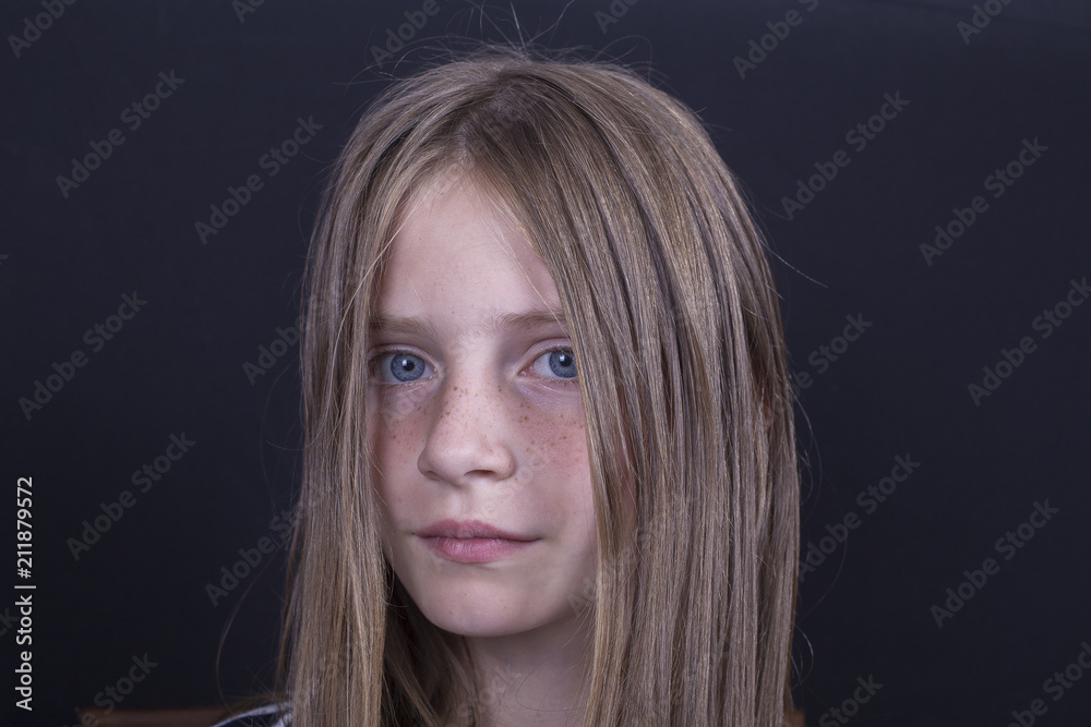 Naklejka premium Beautiful blond young girl with freckles indoors on black background, closeup portrait
