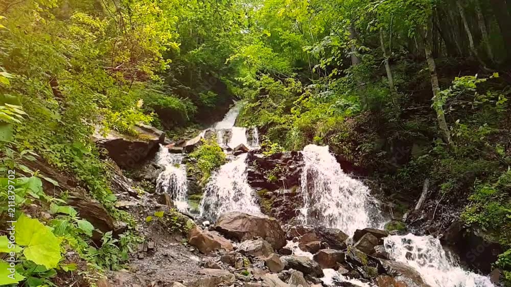 Slow motion of a small mountain waterfall. 240fps. The mountain stream falls down on stones in a bottom. Slow motion of a small mountain waterfall. 240fps. The mountain stream falls down on stones in a bottom.