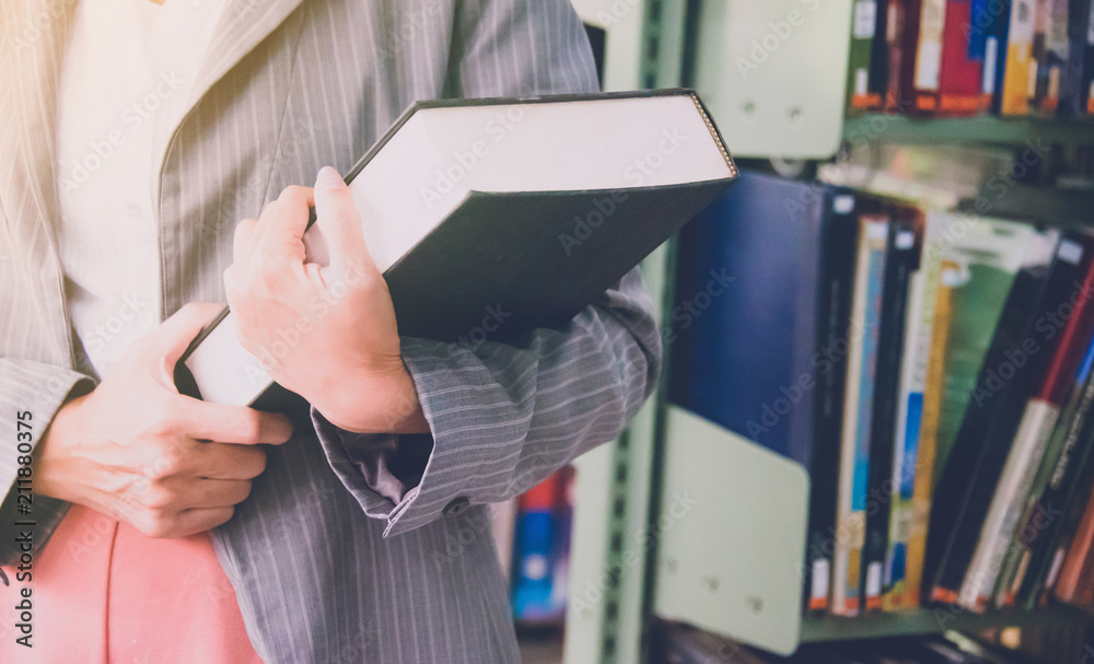 Fototapeta premium Teacher holding text book with soft light morning in library background
