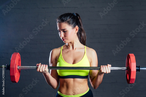 a young woman in a green sports bra and black pants is engaged with a barbell against the backdrop of black bricks