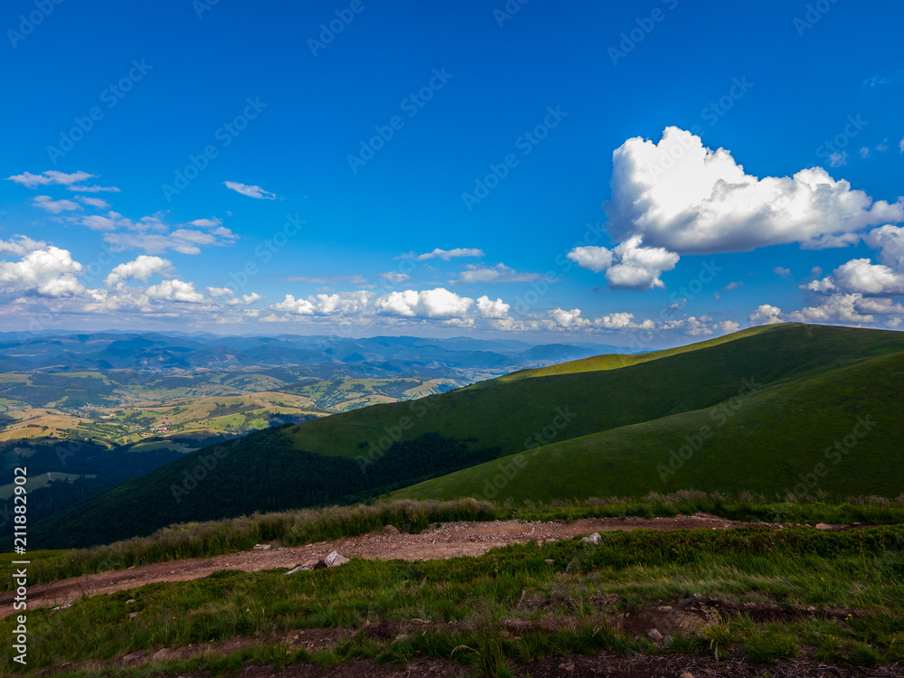 Obraz premium White clouds in the blue sky floating above the mountain peaks stretching to the horizon line