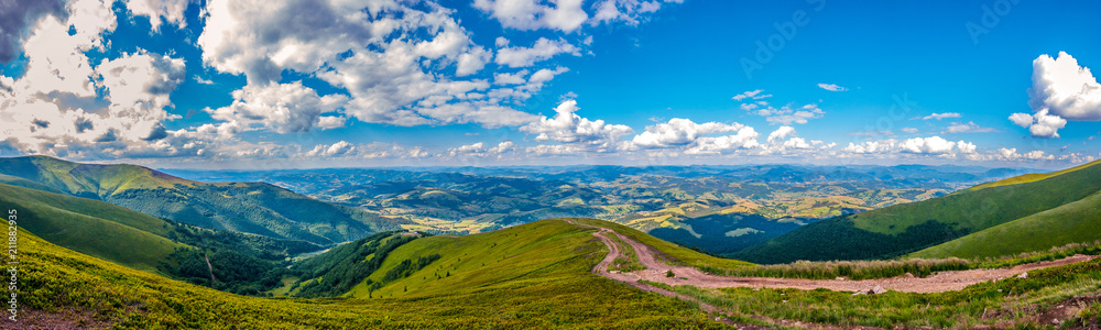 Panoramic view of green hills with mountains, large valleys and blue sky with white clouds on it