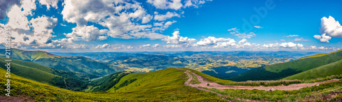Panoramic view of green hills with mountains, large valleys and blue sky with white clouds on it